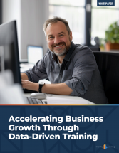 The cover of the white paper "Accelerating Business Growth Through Data-Driven Training" showing a happy trainer at a desk in front of a desktop monitor